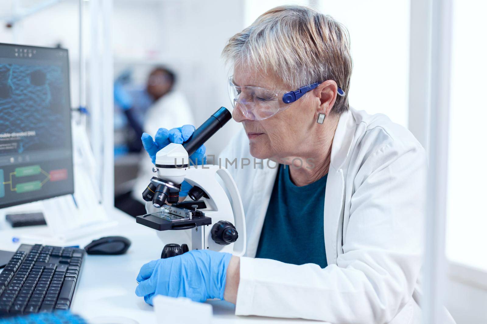 Senior chemist scientist doing genetic investigation using microscope. Elderly researcher carrying out scientific research in a sterile lab using a modern technology.