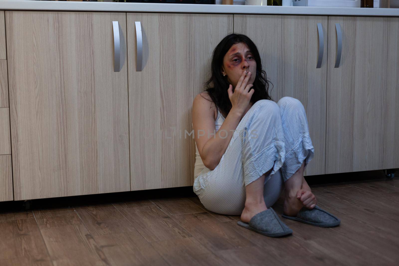 Close up of crying wife being victim of physical trauma and domestic violence. Miserable woman with bruises on face sitting on floor unhappy with aggressive husband and marriage
