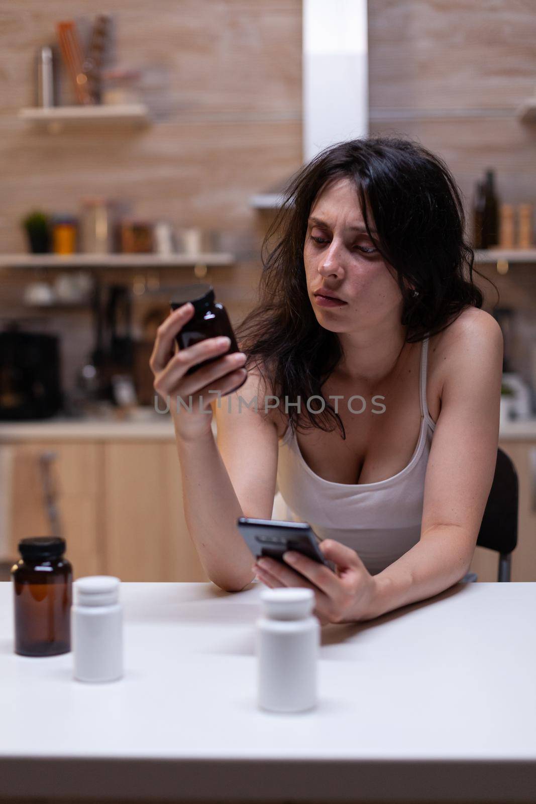 Sick woman with migraine looking at container with medicine by DCStudio