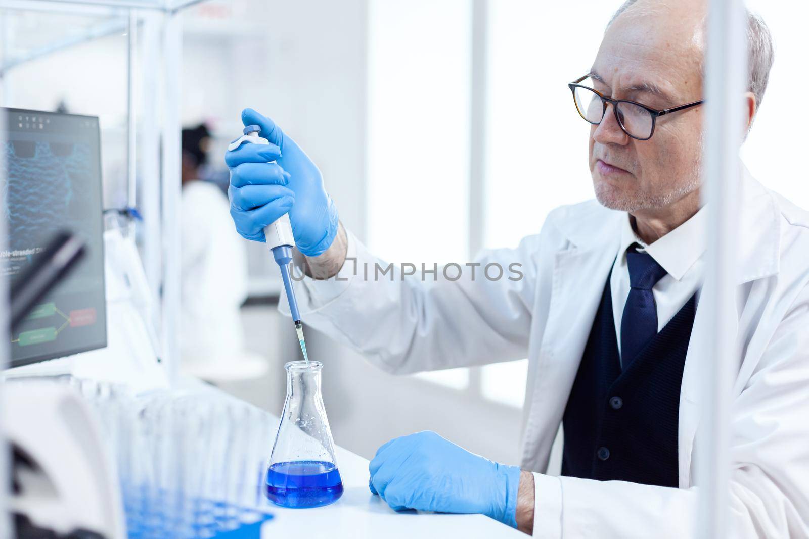 Experienced scientist working in biotechnological laboratory with sterile dropper and blue liquid. Senior professional chemist using pippete with blue solution for microbiology tests.