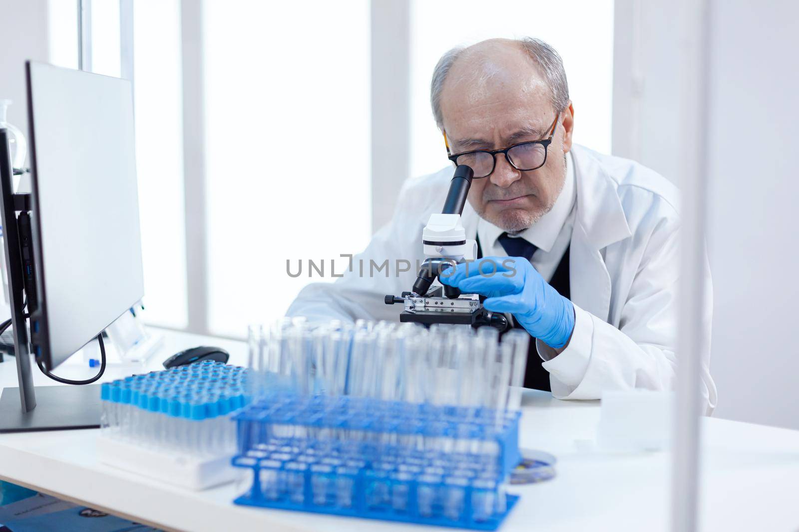 Healthcare senior scientist man in medical industry carrying out genetic analysis using microscope. Chemist researcher in sterile lab doing experiments for medical industry using modern technology.