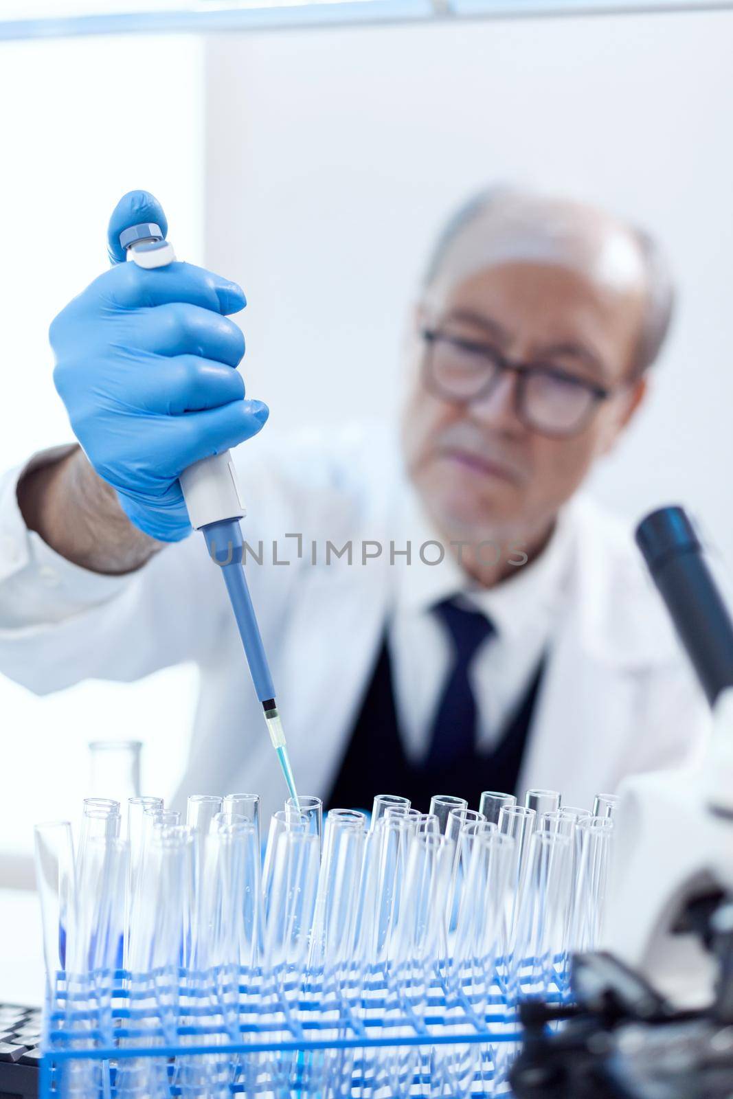 Scientist with protection gear using dropper pipette engineering vaccine treatment. Senior professional chemist using pippete with blue solution for microbiology tests.