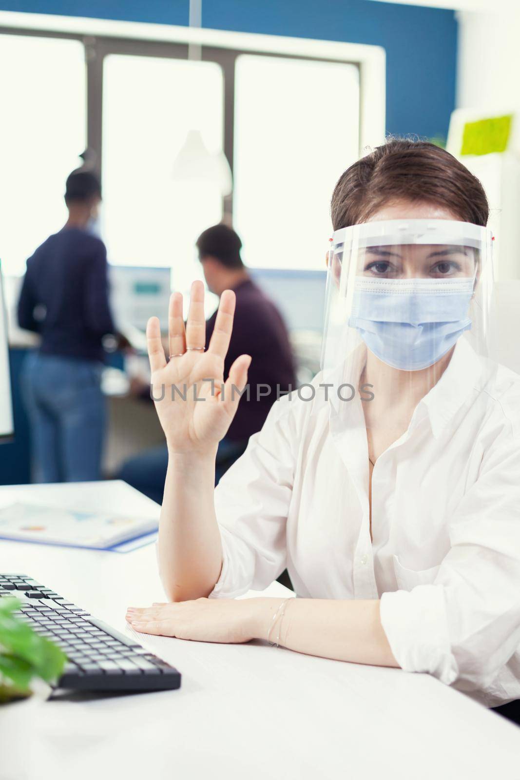 Entrepreneur having virtual conference with business person from company office wearing face mask. Pov of manager speaking with remotely team during online call while colleagues working in background.