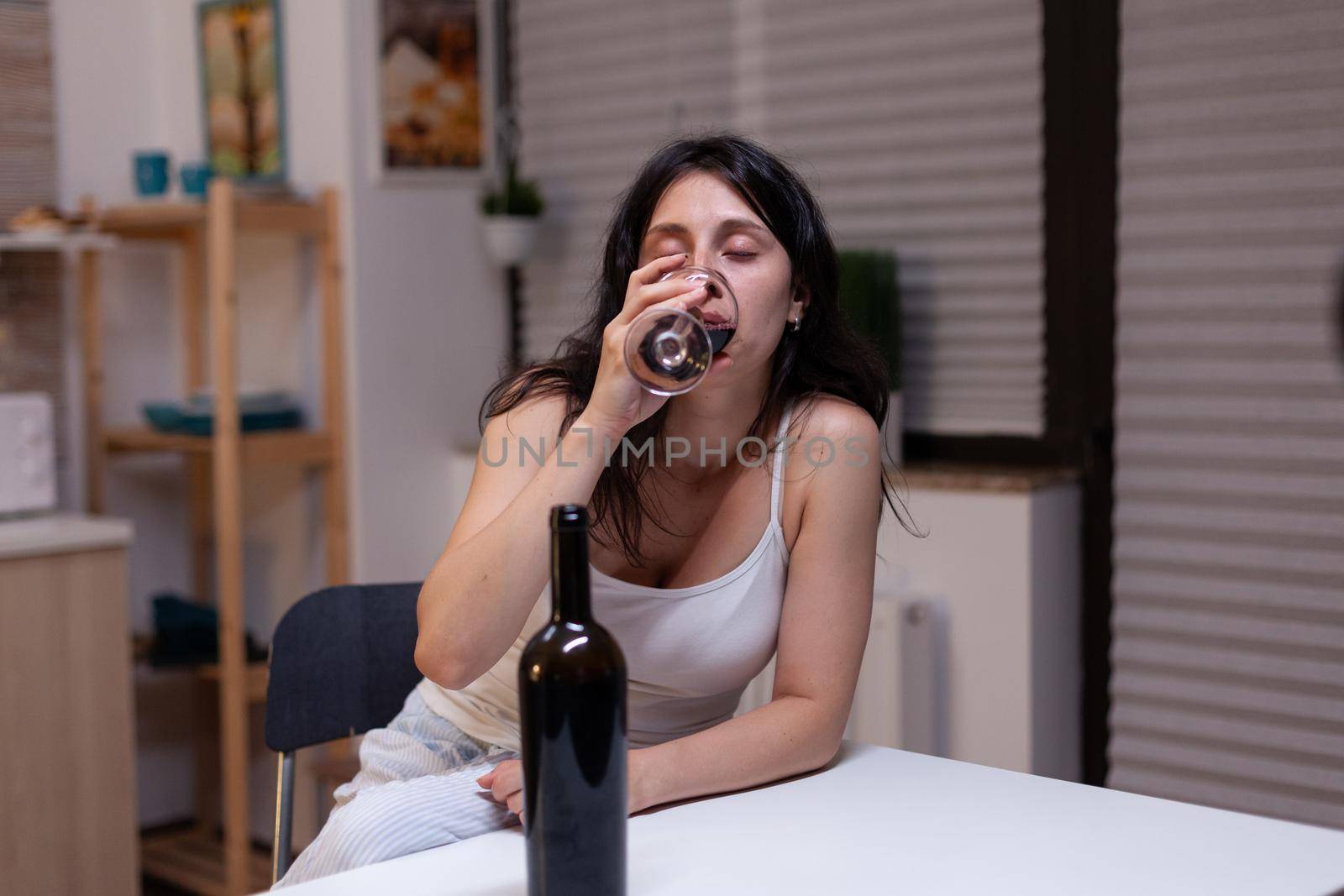 Unhappy woman with alcohol addiction drinking wine alone by DCStudio