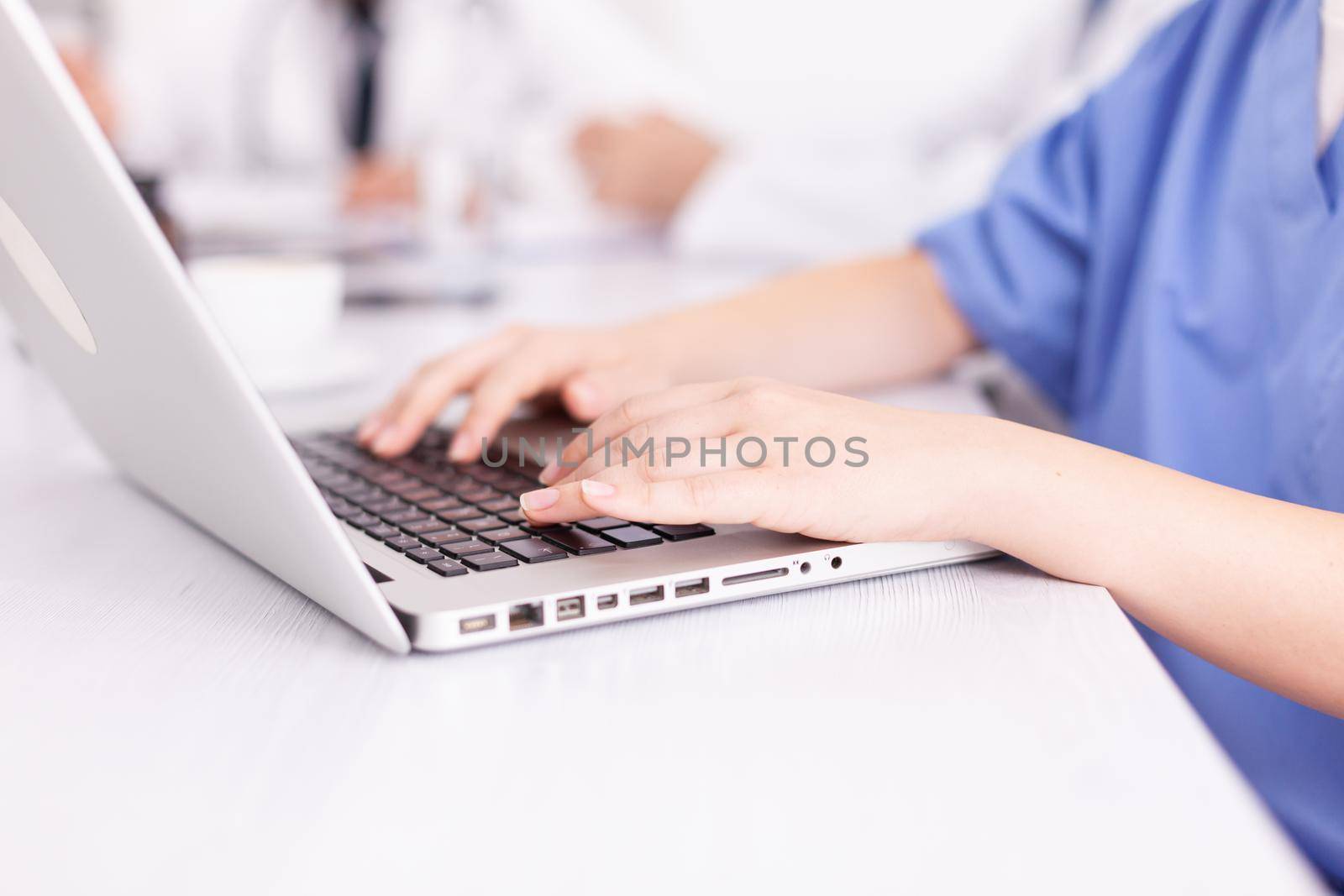 Close up of medical nurse typing on laptop during healtchare meeting with coworkers in hospital boardroom. Clinic expert therapist talking with colleagues about disease, medicine professional