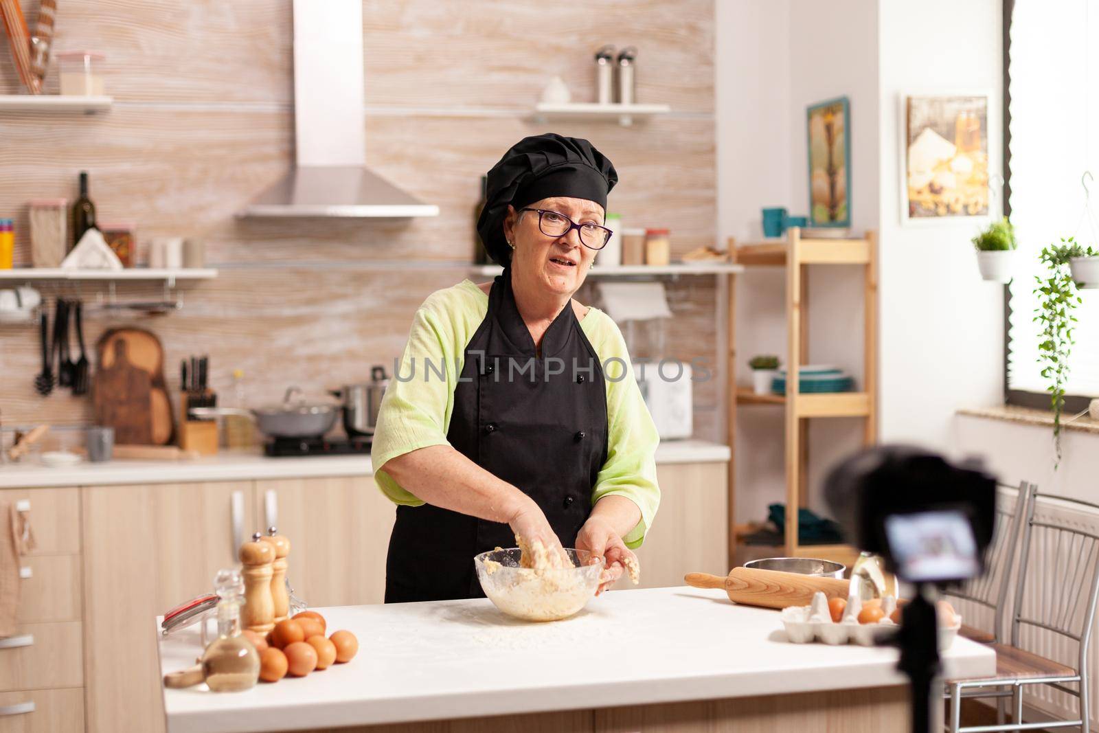 Aged female vlogger making social media video about cooking for the internet channel. Retired blogger chef influencer using internet technology communicating, shooting blogging on social media with digital equipment