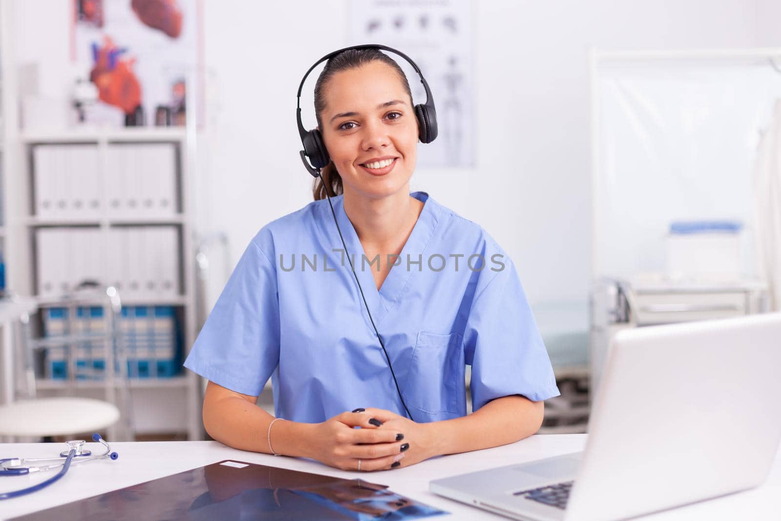 Young practitioner doctor working at the clinic reception desk talking with patients wearing headphones. Female nurse, doctor having a conversation with sick person during consultation, medicine.