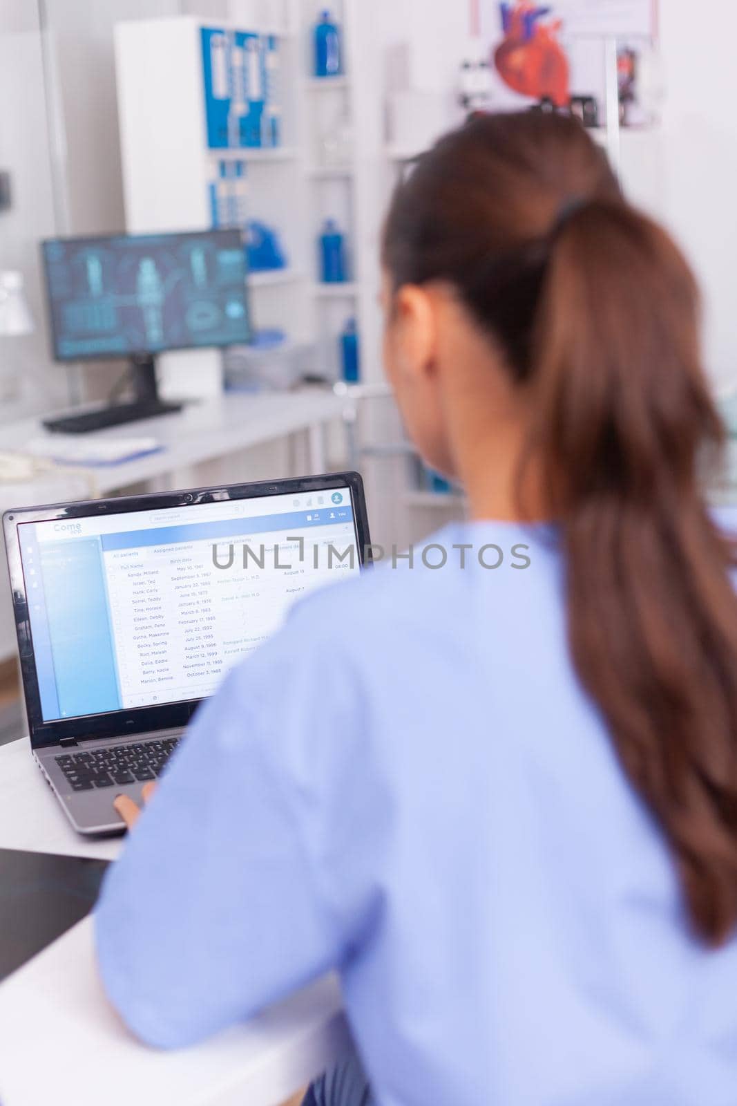 Medical practitioner looking at patients forms and contracts of health care. Healthcare physician using computer in modern clinic looking at monitor, medicine, profession, scrubs.
