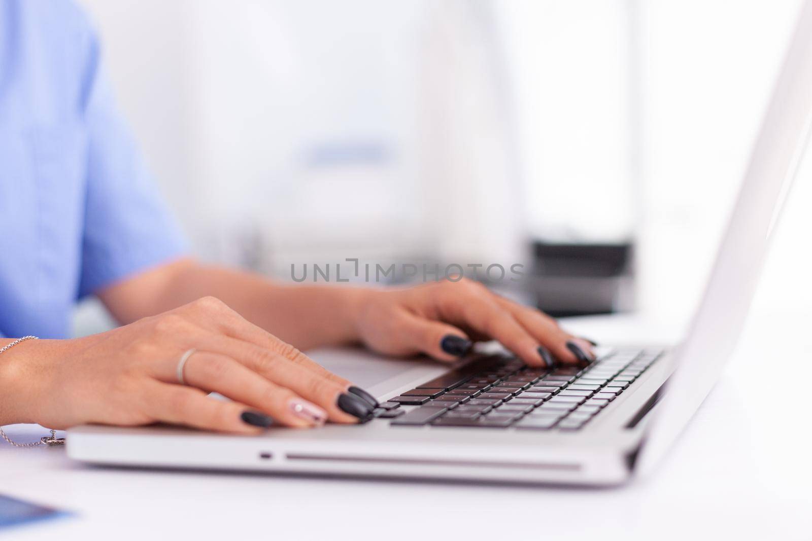 Close up of doctor hands typing on a laptop in a medical office. Health practitioner searching in hospital database using laptop in hospital cabinet, keyboard, job.