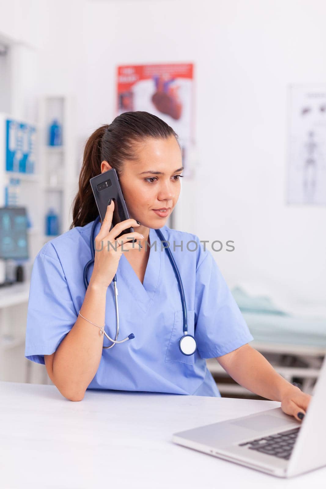 Medical receptionist talking with patient in hospital office and using laptop . Health care physician sitting at desk using computer in modern clinic looking at monitor.