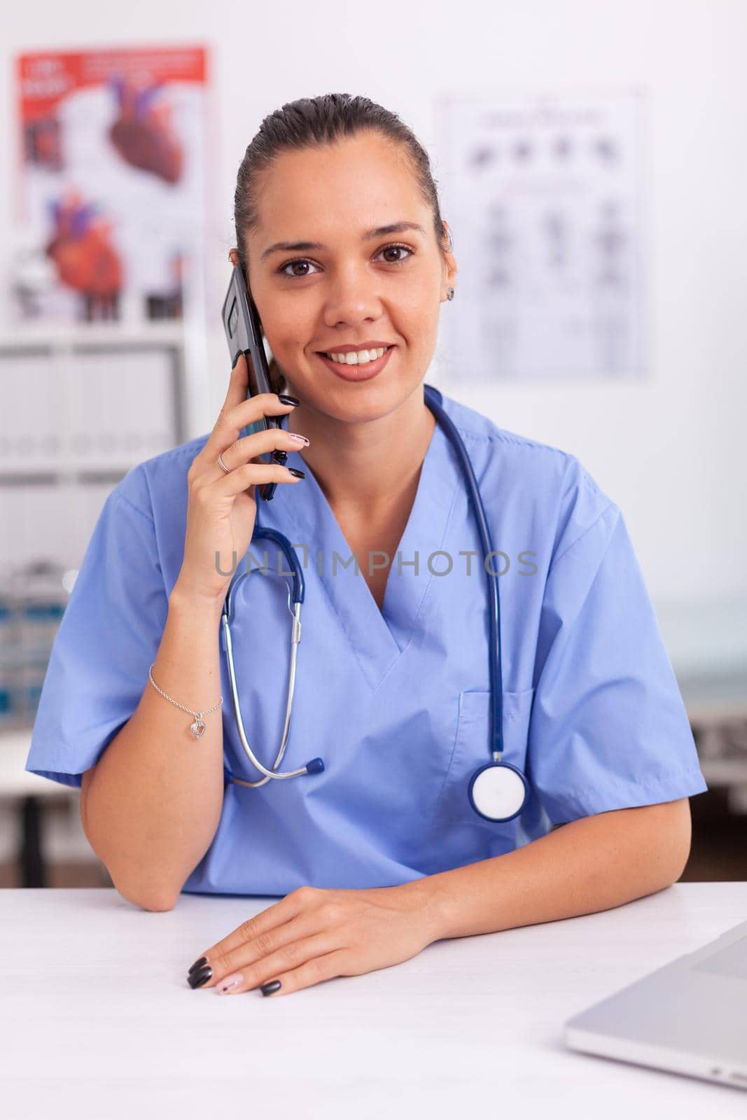 Medical staff talking with patient on phone from hospital office about diagnosis smiling at camera. Female nurse, doctor having a phone conversation with sick person during consultation, medicine.