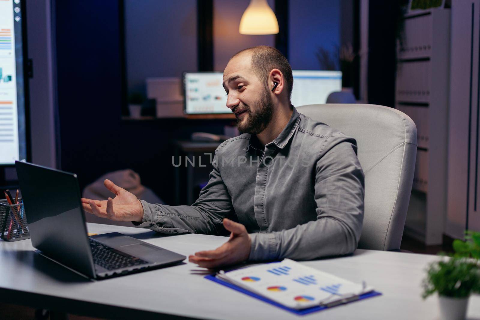 Freelancer uses wireless headphone to talk with people on online call. Businessman in the course of an important video conference while doing overtime at the office.