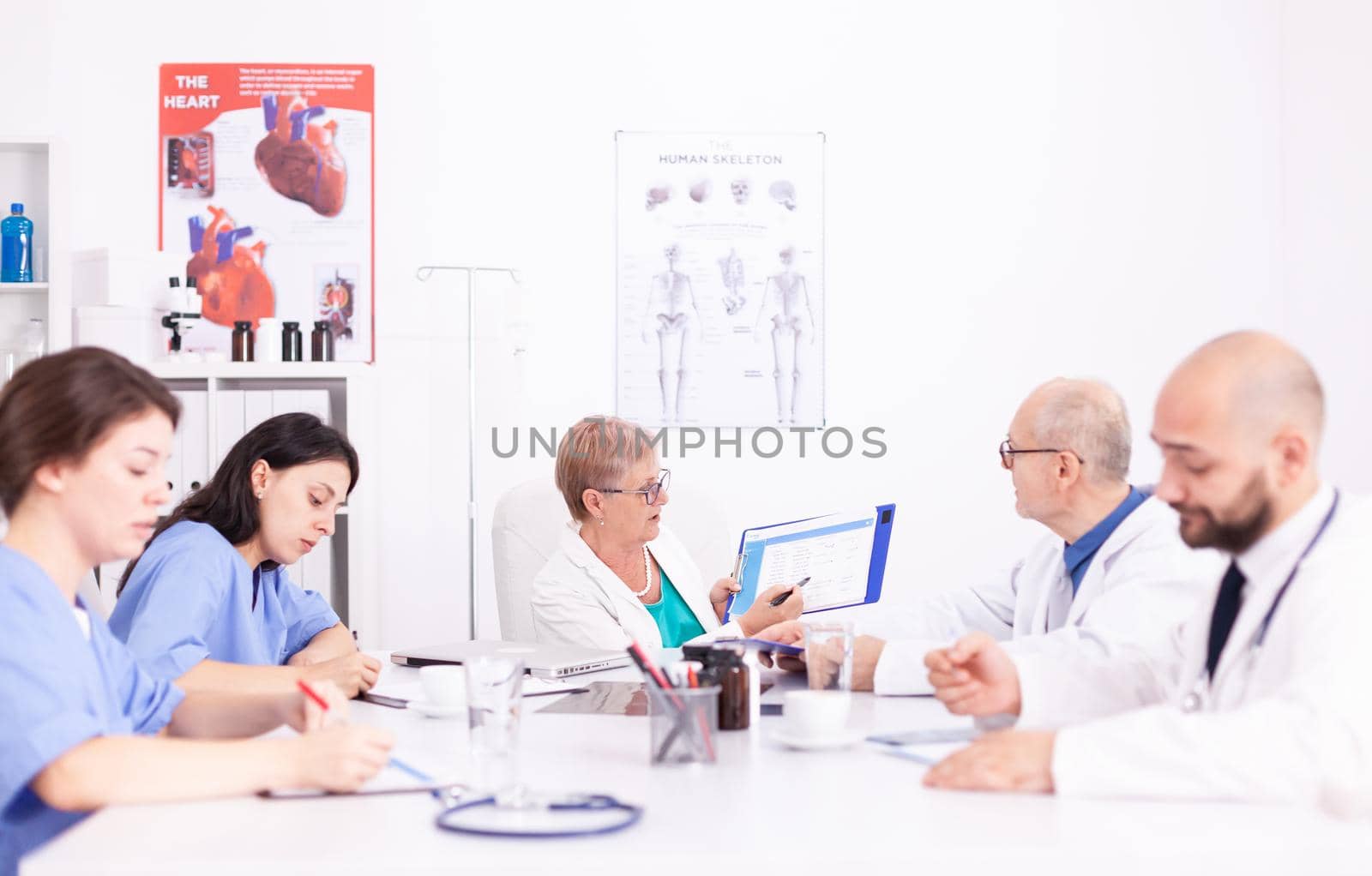Female nurses taking notes while medical expert explaining about viral diseases in hospital conference room. Clinic expert therapist talking with colleagues about disease, medicine professional