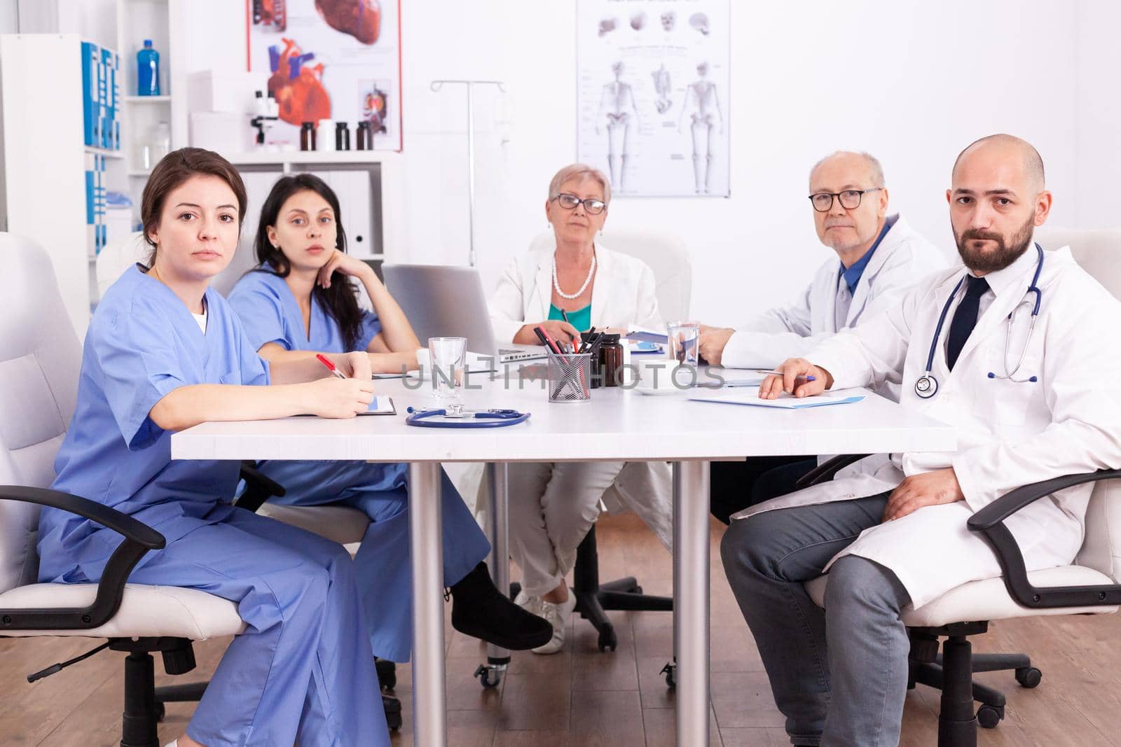 Portrait of medical team looking at camera sitting at desk in conference room. Clinic expert therapist talking with colleagues about disease, medicine professional