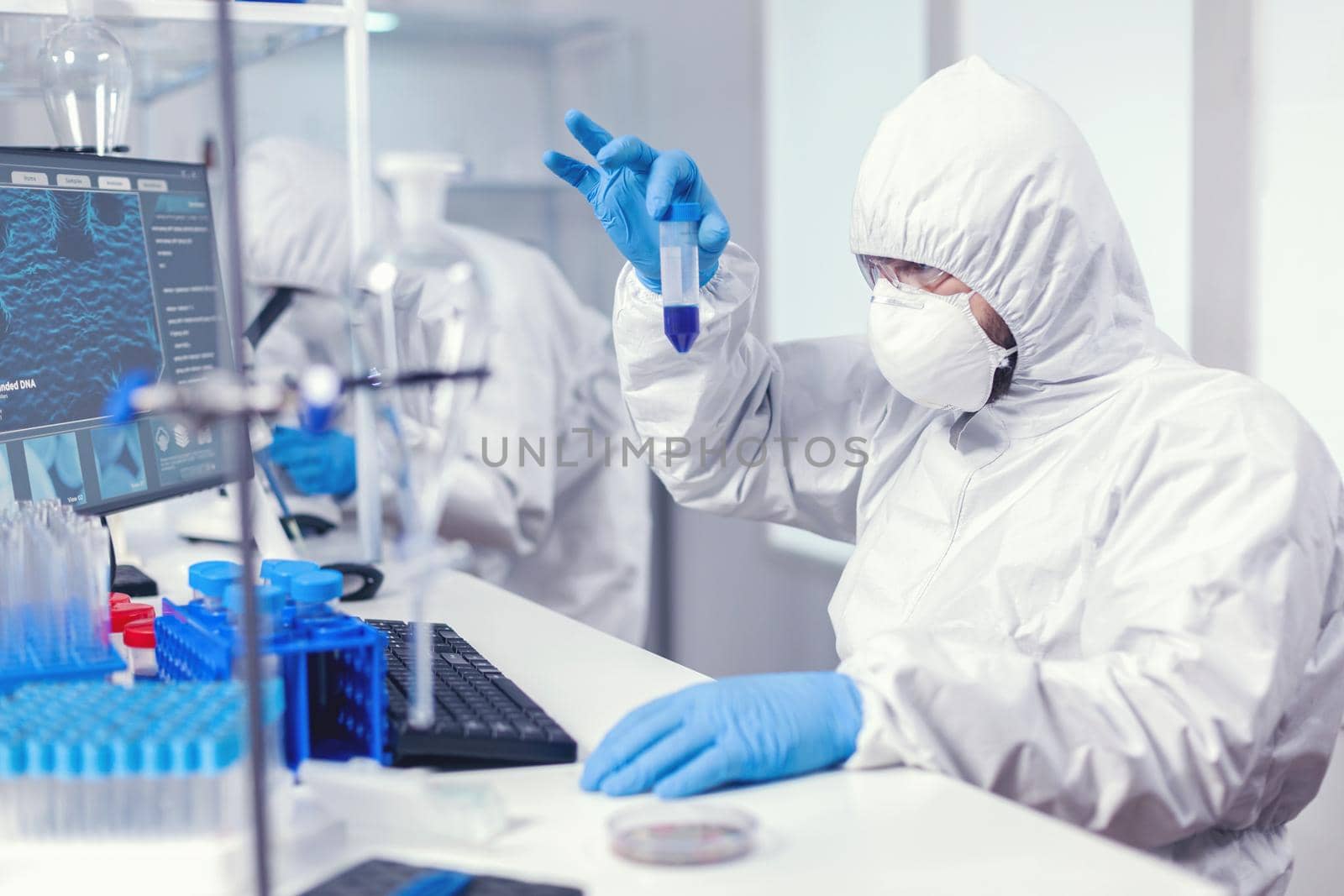 Scientist in lab coversall looking closely at sample in test tube in the course of coroanvirus. Researcher in laboratory wearing coverall doing research and analyzing substance during global pandemic with covid19.