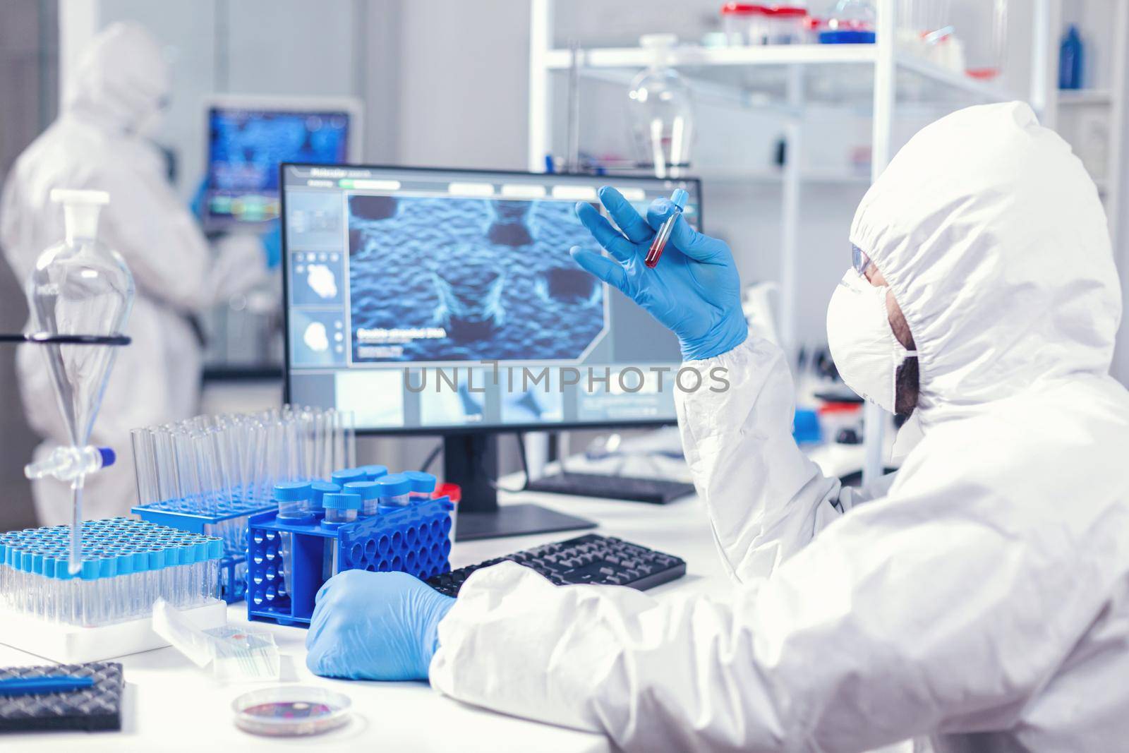 Scientist in sterile chemistry suit analysing blood sample from test tube. Doctor working with various bacteria and tissue, pharmaceutical research for antibiotics against covid19.