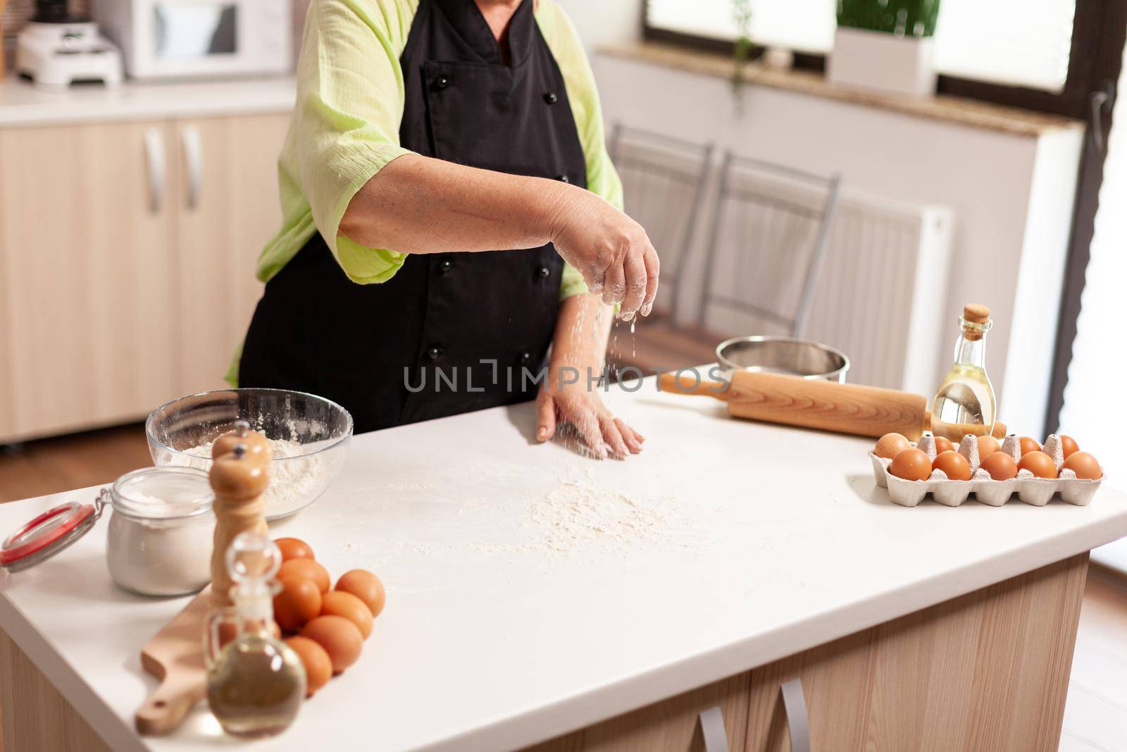 Process of preparing the dough for homemade bread. Retired senior chef with bonete and apron, in kitchen uniform sprinkling sieving sifting ingredients by hand baking homemade pizza and bread