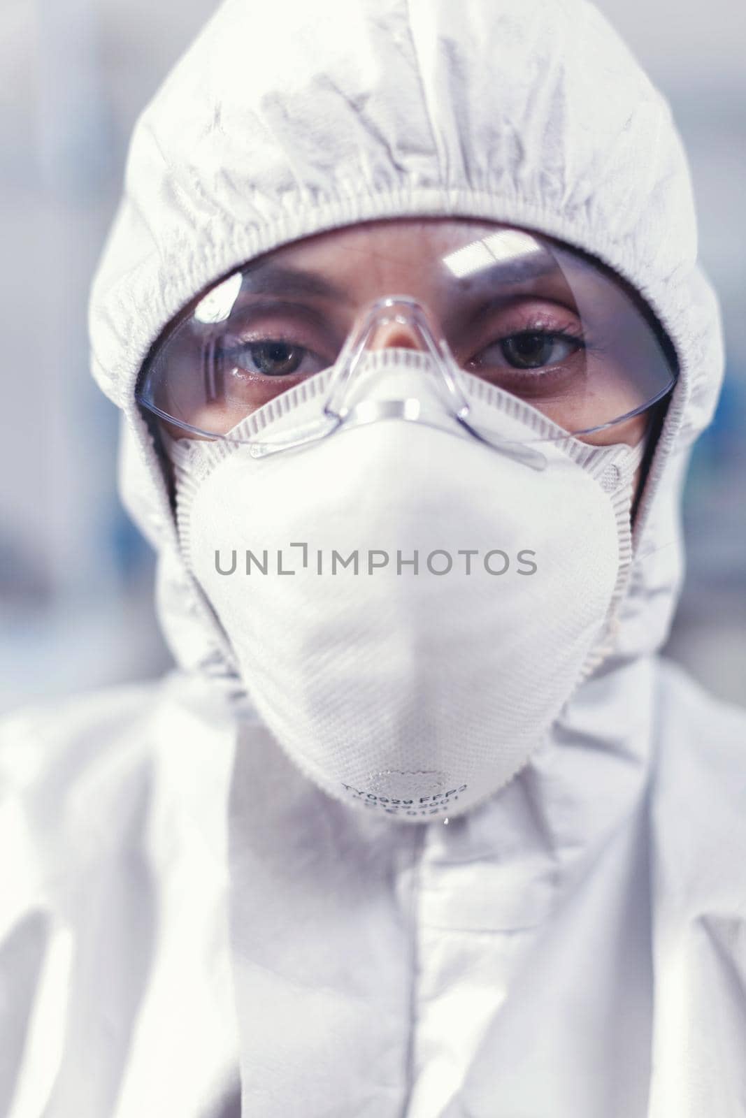 Close up of scientist woman dressed in coverall sitting at workplace in laboratory. Tired woman scientist in biotechnology laboratory wearing protective suit during global epidemic.