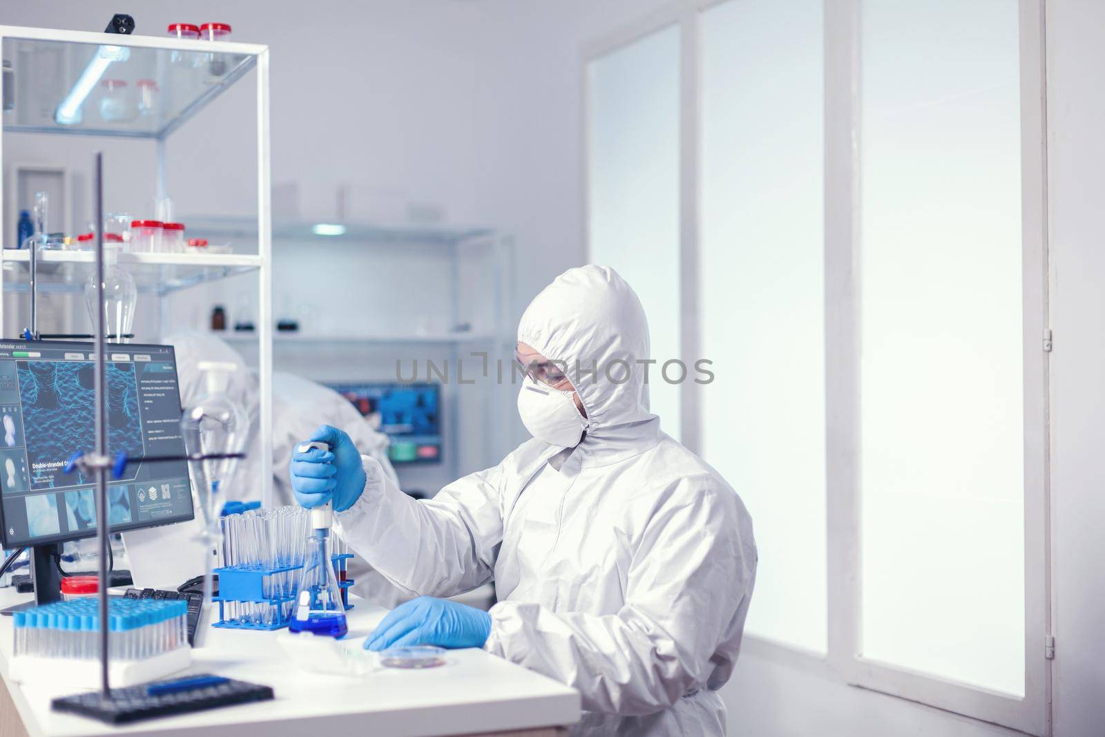 Medical worker uses micropipette in modern scientific facility wearing protection suit as safety precaution. Chemist in modern laboratory doing research using dispenser during global epidemic with covid-19.