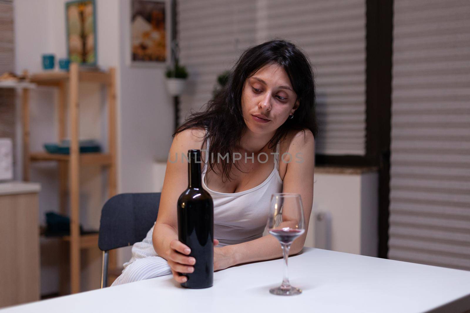 Unhappy woman with alcohol addiction drinking wine alone feeling depressed and intoxicated. Young adult with bottle of wine and glass using liquor for sadness, loneliness and desperation