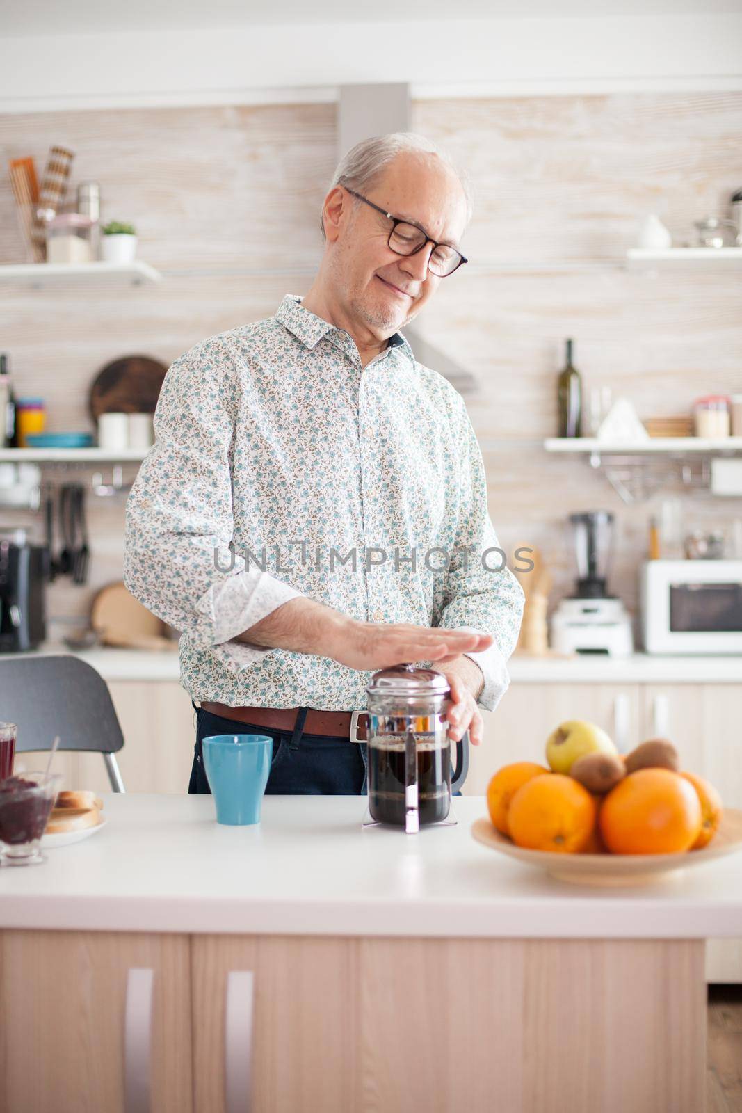 Happy senior man pushing on french press while preparing coffee for breakfast. Elderly person in the morning enjoying fresh brown cafe espresso cup caffeine from vintage mug, filter relax refreshment