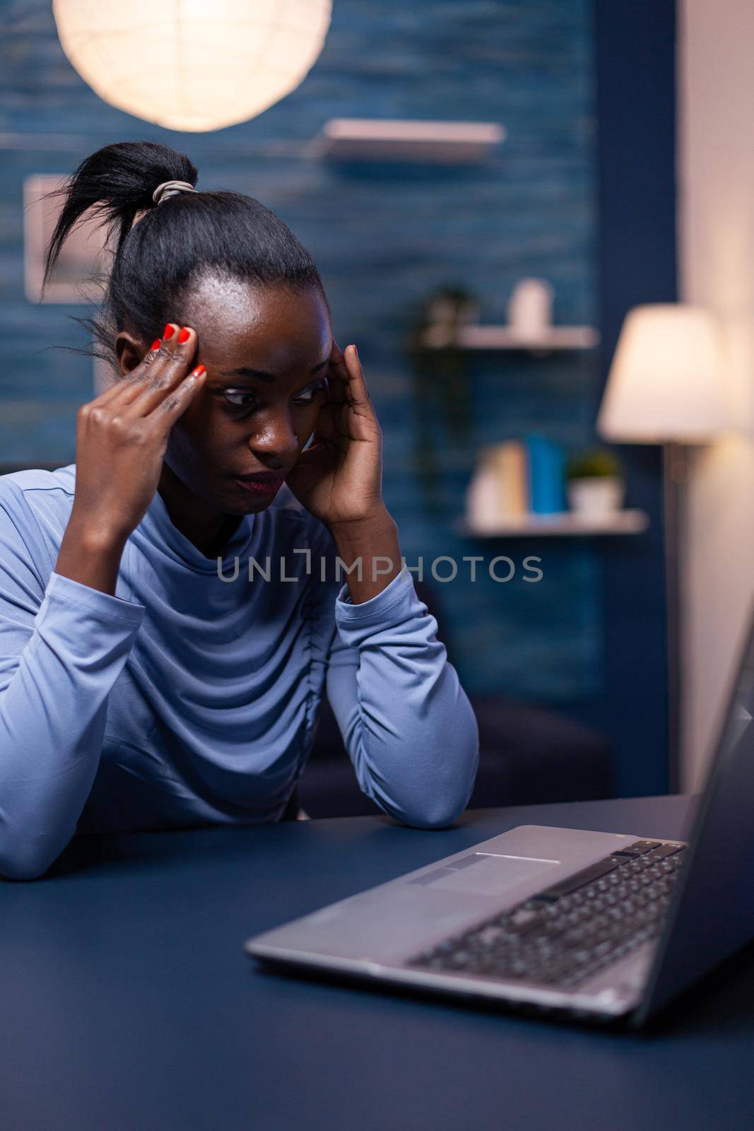Overworked african business woman having a headache while working late in the night from home office. Tired focused employee using modern technology network wireless doing overtime.