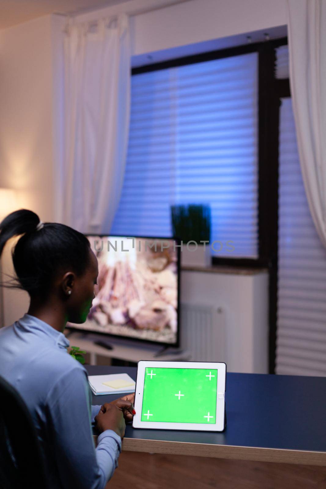 African entrepreneur sitting at desk in home office holding tablet pc with green screen working on deadline. Using mockup chroma key display computer.