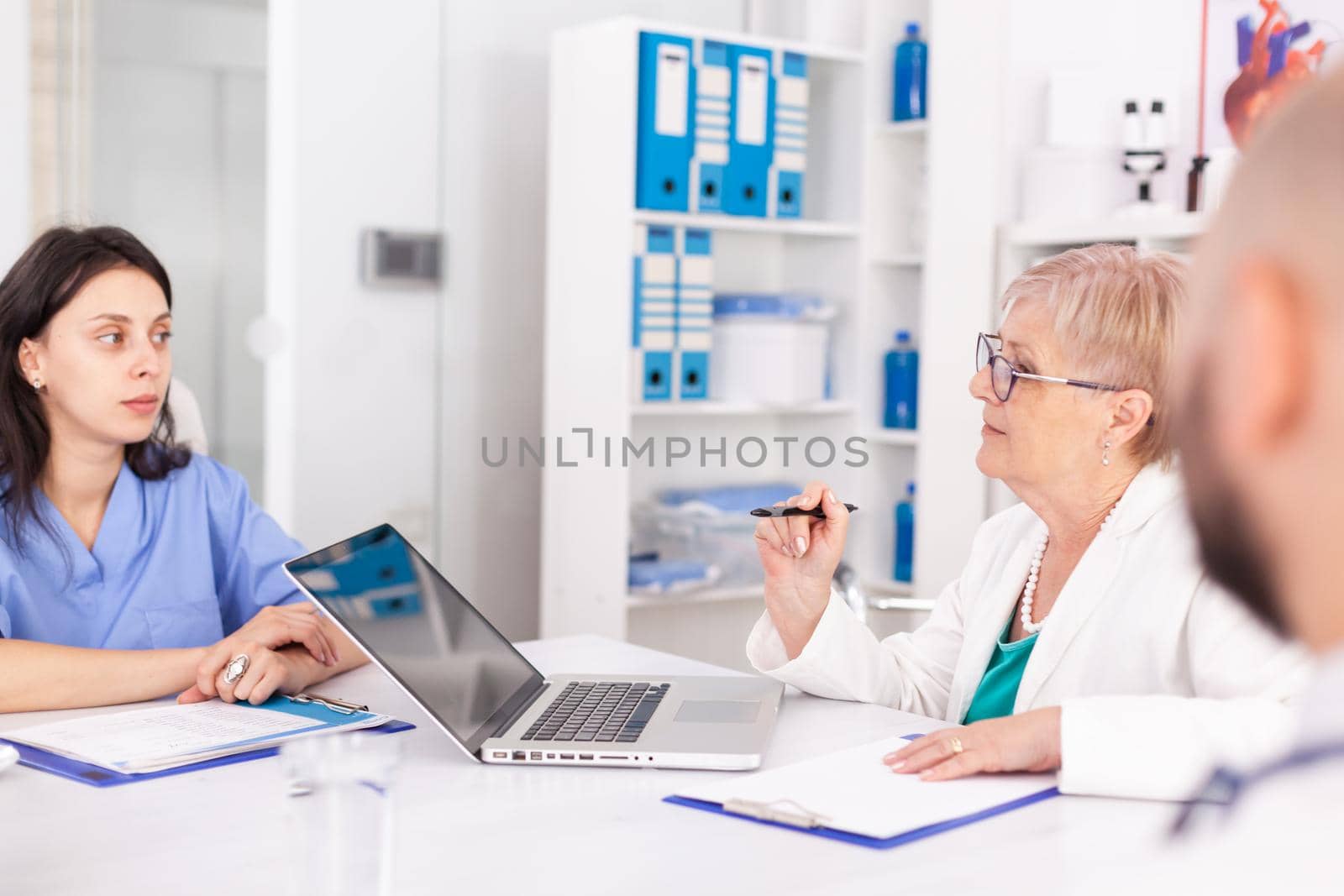 Mature doctor talking about patient diagnosis during meeting with her medical staff. Clinic therapist with colleagues talking about disease, expert,specialist, communication.