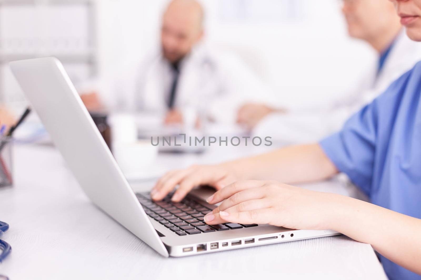 Medical practitioner typing diagnosis on laptop during briefing with coworkers. Clinic expert therapist talking with colleagues about disease, medicine professional