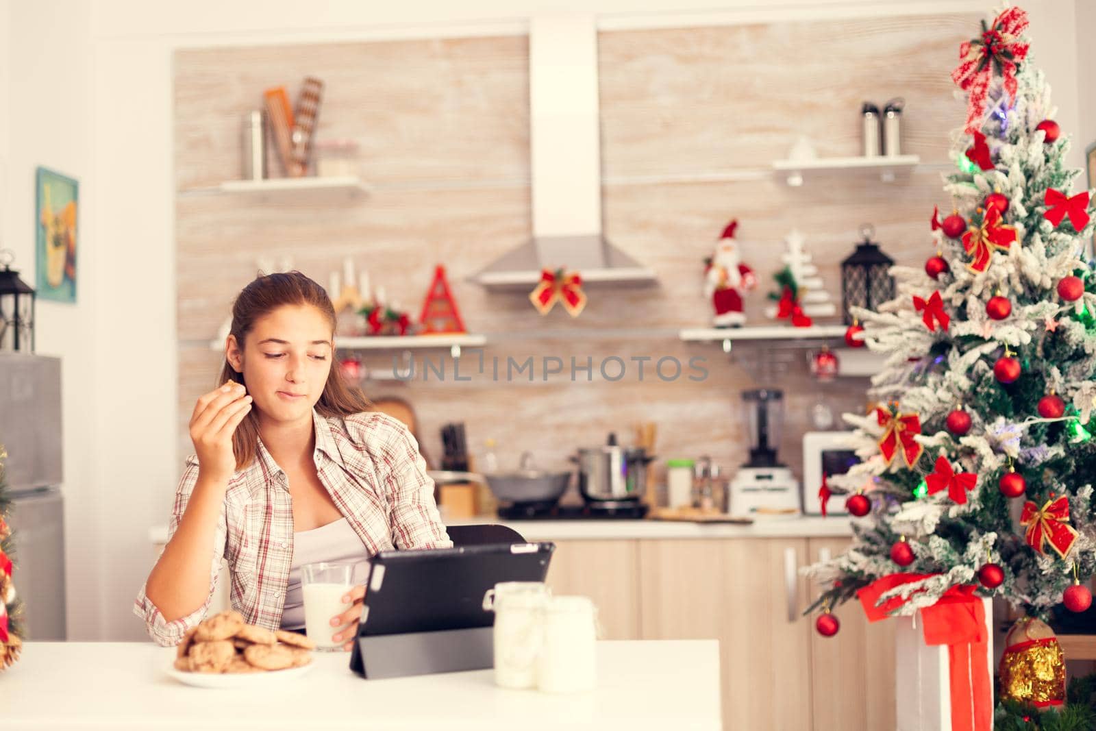 Grandchild eating cookies on christmas day with x-mas tree in the background by DCStudio
