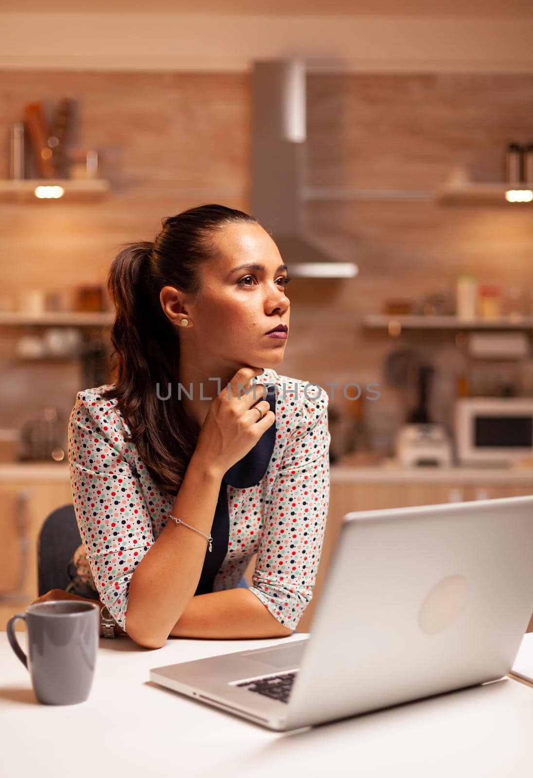 Concentrated businesswoman in home kitchen while working late at night on laptop. Employee using modern technology at midnight doing overtime for job, business, busy, career, network, lifestyle.
