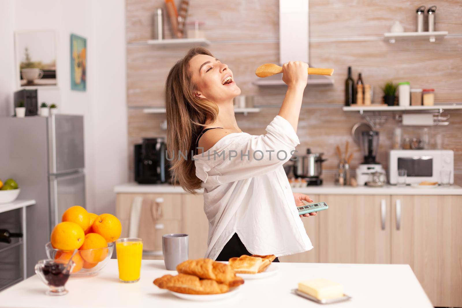 Woman singing during breakfast in home kitchen wearing sexy lingerie. Seductive woman with tattoos using smartphone wearing temping underwear in the morning.