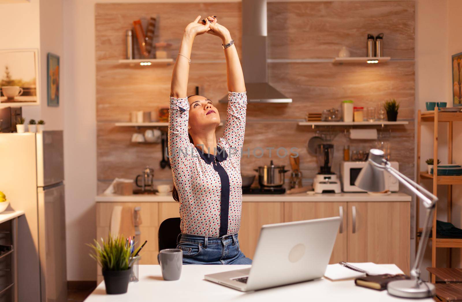 Tired businesswoman streching while working overtime from home kitchen. Employee using modern technology at midnight doing overtime for job, business, busy, career, network, lifestyle ,wireless.