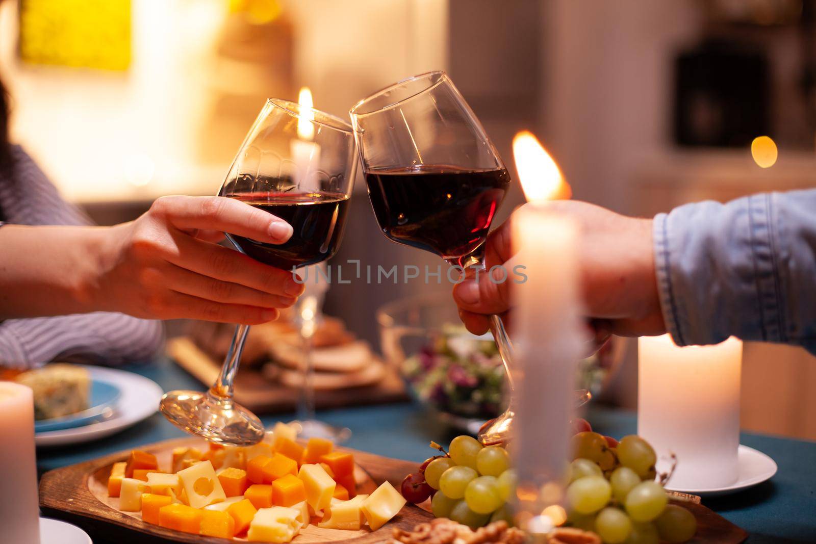 Romantic celebrating relationship toasting with red wine. Happy cheerful young couple dining together in the cozy kitchen, enjoying the meal, celebrating anniversary romantic toast.