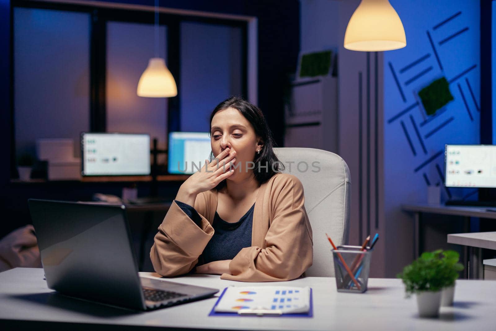 Sleepy businesswoman yawns while working on laptop by DCStudio