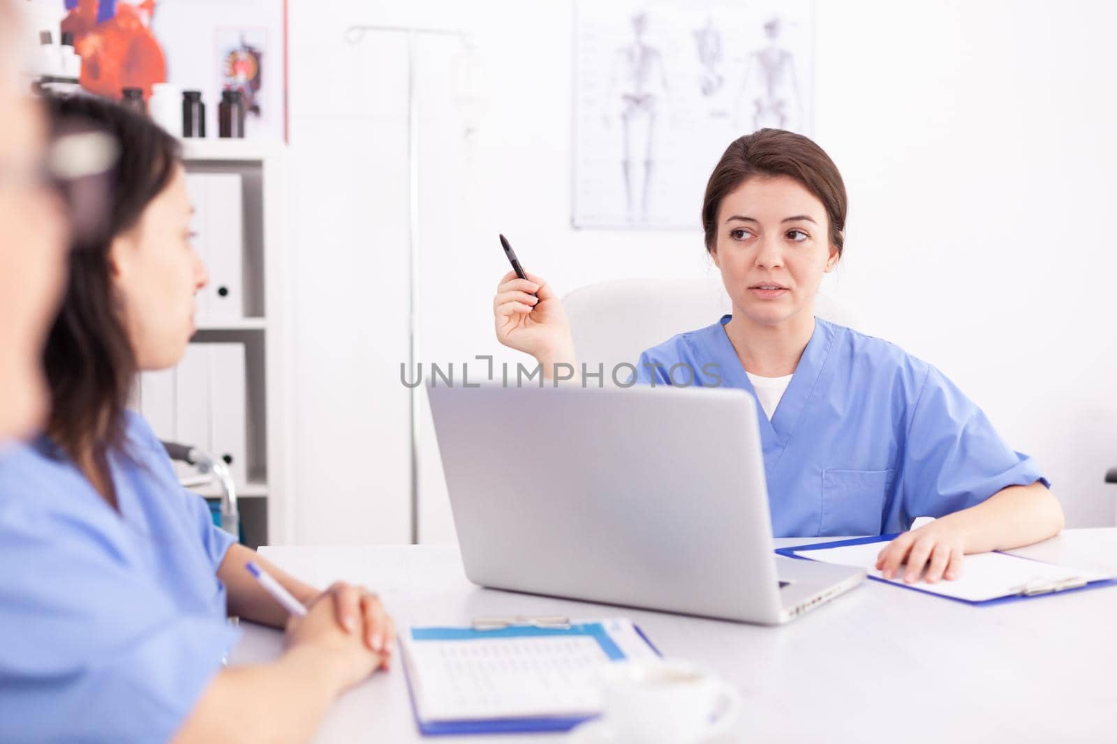 Medical nurse using laptop during briefing with medicine experts in hospital conference room. Clinic therapist with colleagues talking about disease, expert,specialist, communication.