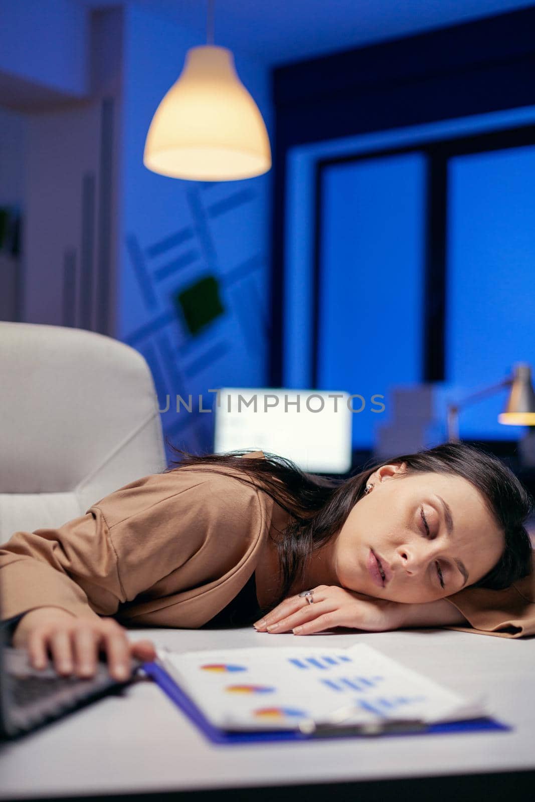 Portrait of overworked businesswoman sleeping desk in corporate office. Employee falling asleep while working late at night alone in the office for important company project.