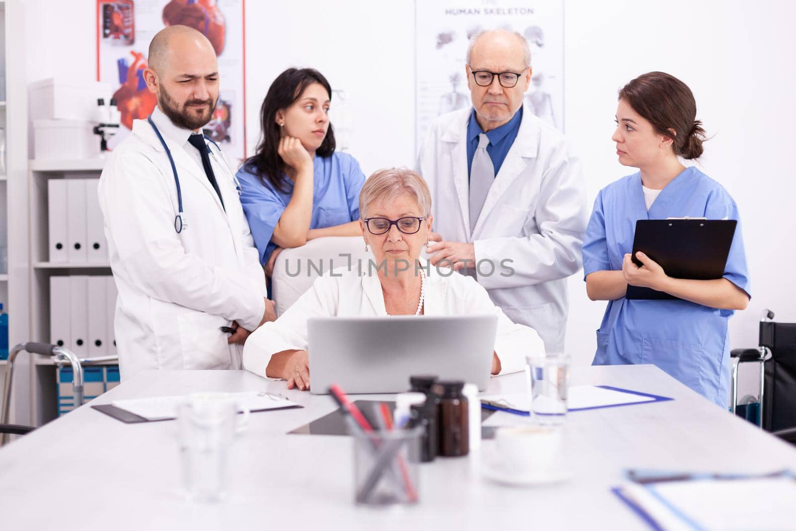 Mature doctor specialist briefing her medical team in conference room using laptop. Clinic expert therapist talking with colleagues about disease, medicine professional