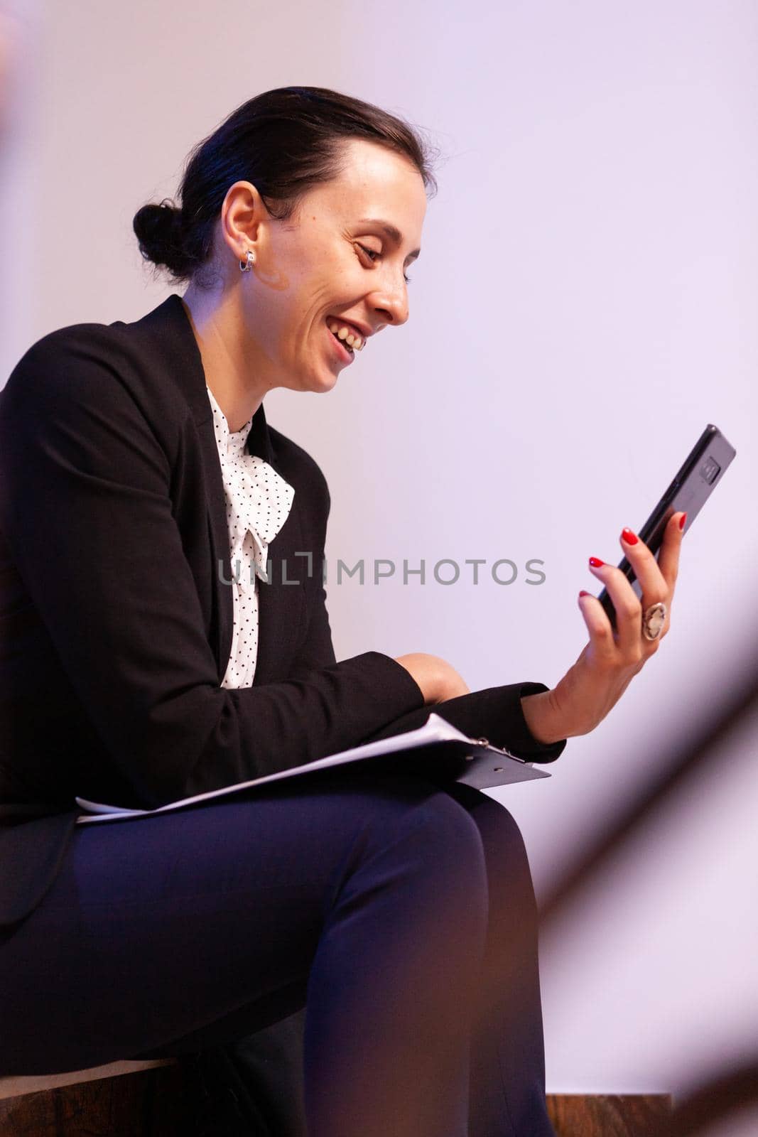 Overworked businesswoman smiling during video call about project deadline. Entrepreneur talking with client using smartphone for video call sitting on stairs.