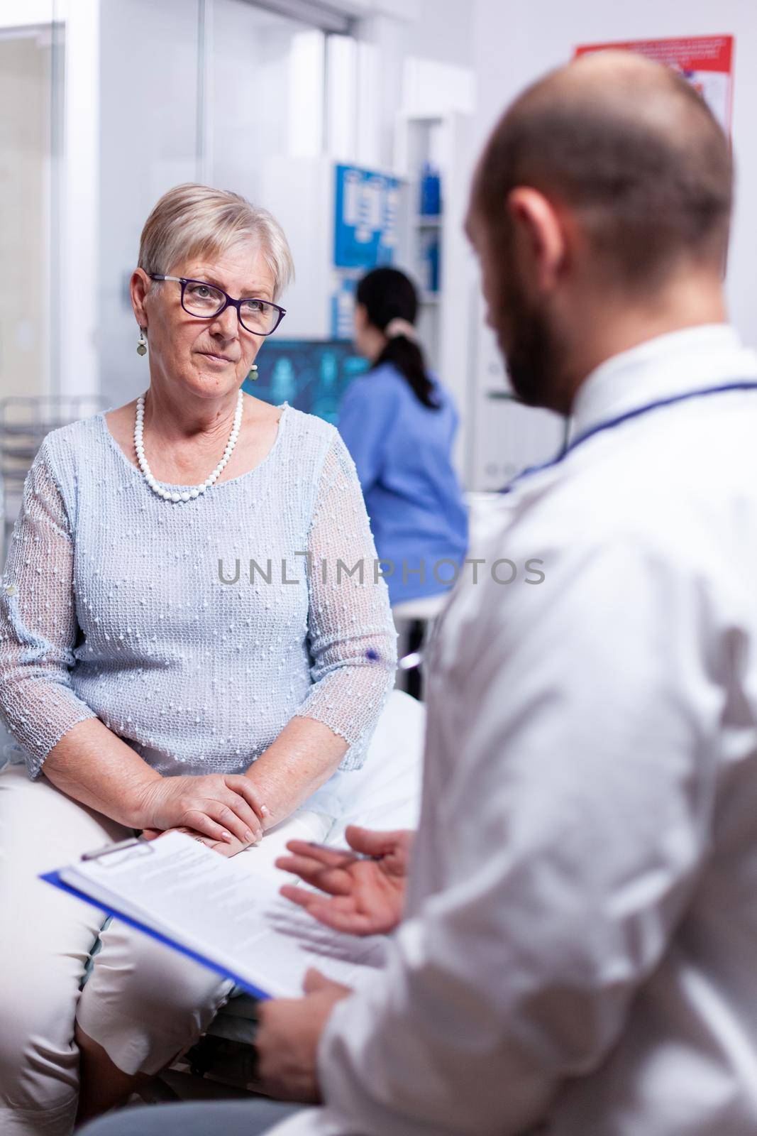 Doctor explaining diagnosis to retired old woman in hospital room. Converstation with medical stuff clinic medicine healthcare, senior, coat, clipboard.