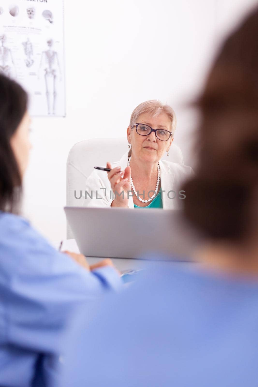 Mature medical physician explaining treatment to nurses during healthcare seminar. Clinic therapist with colleagues talking about disease, expert,specialist, communication.