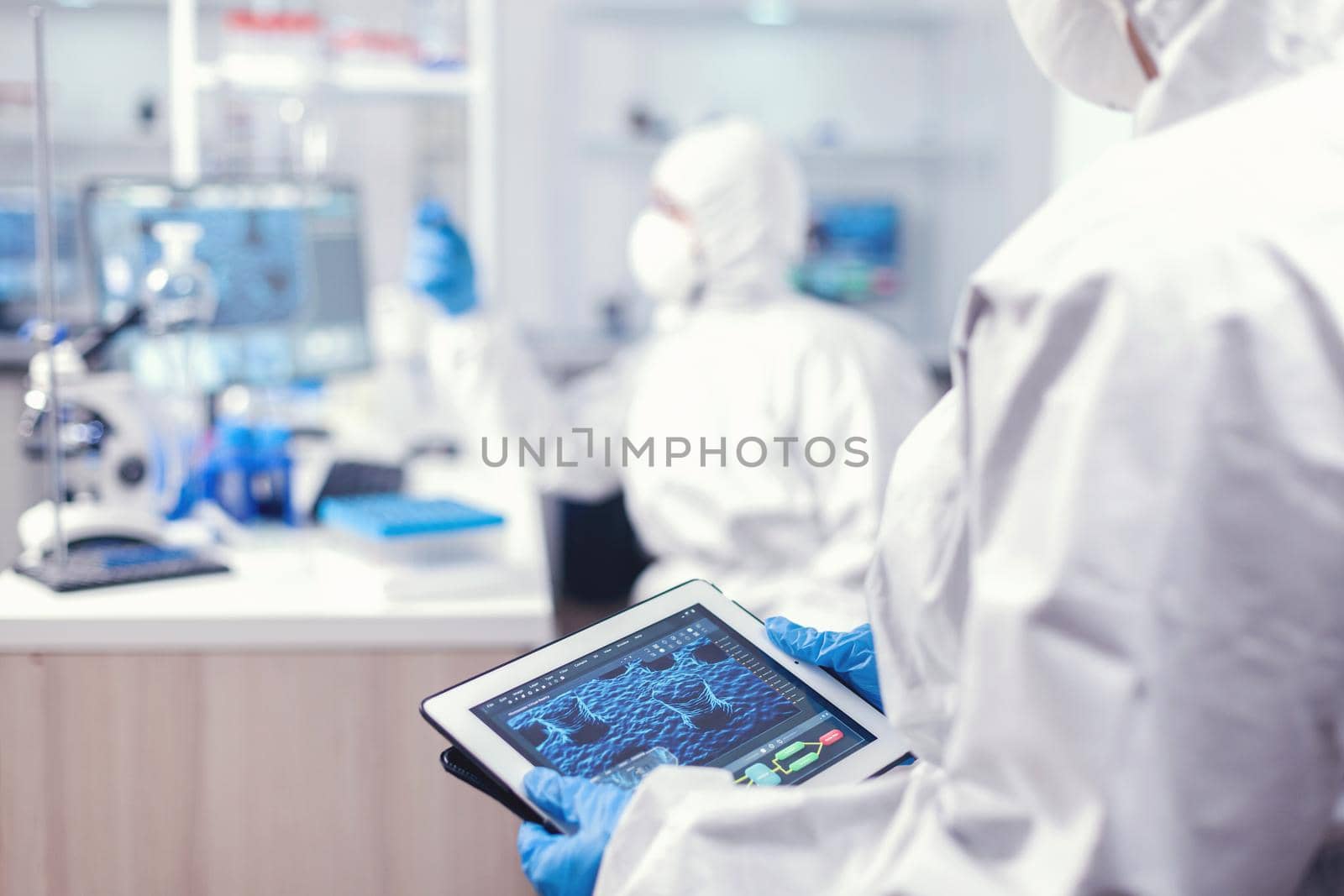 Medical engineer developing vaccine for coronavirus using tablet pc wearing ppe suit. Team of scientists conducting vaccine development using high tech technology for researching treatment against covid19