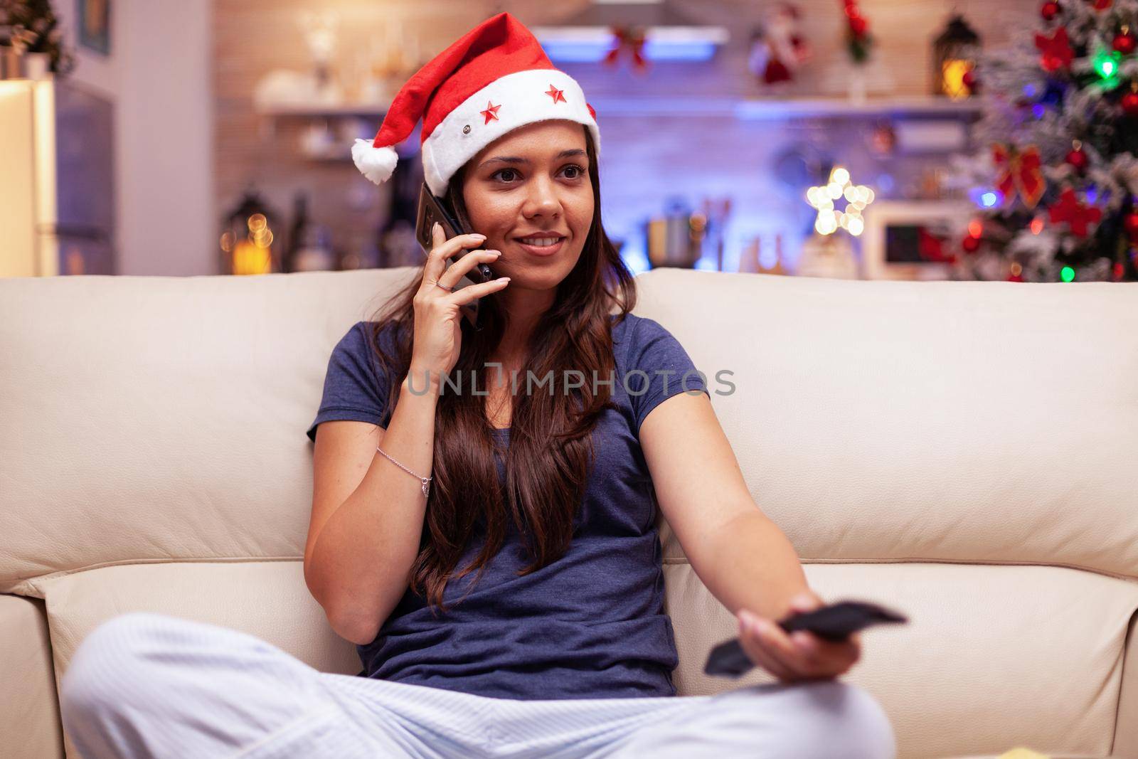 Smiling woman talking with friend at phone watching xmas movie relaxing in x-mas decorated kitchen during christmastime. Caucasian female enjoying winter season celebrating christmas holiday