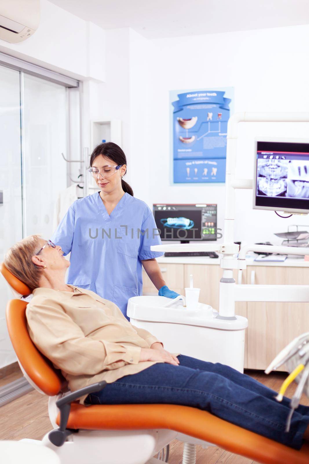 Assistant in dental clinic questioning elderly patient by DCStudio