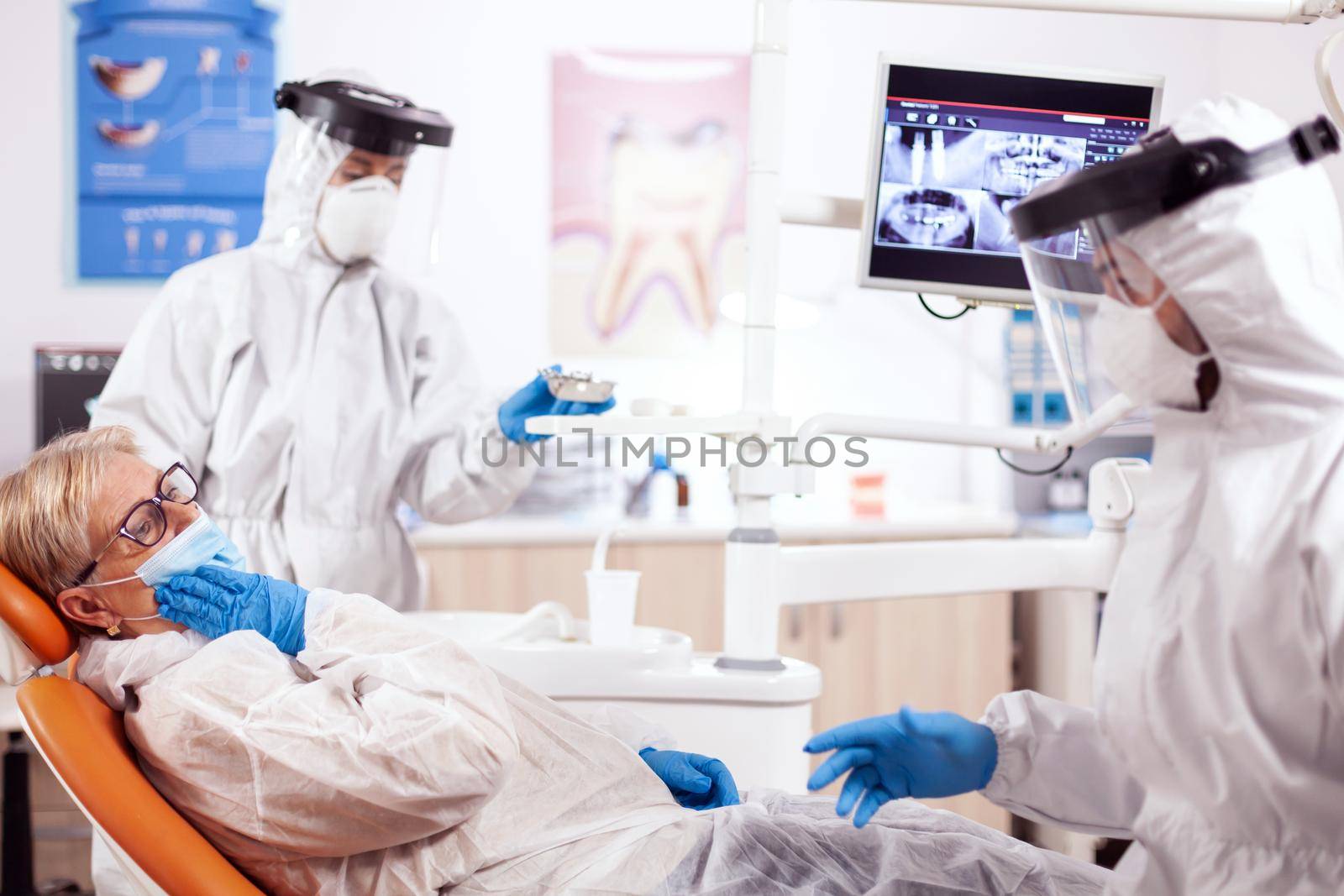 Senior patient presenting teeth pain wearing hazmat suit agains coronavirus by DCStudio