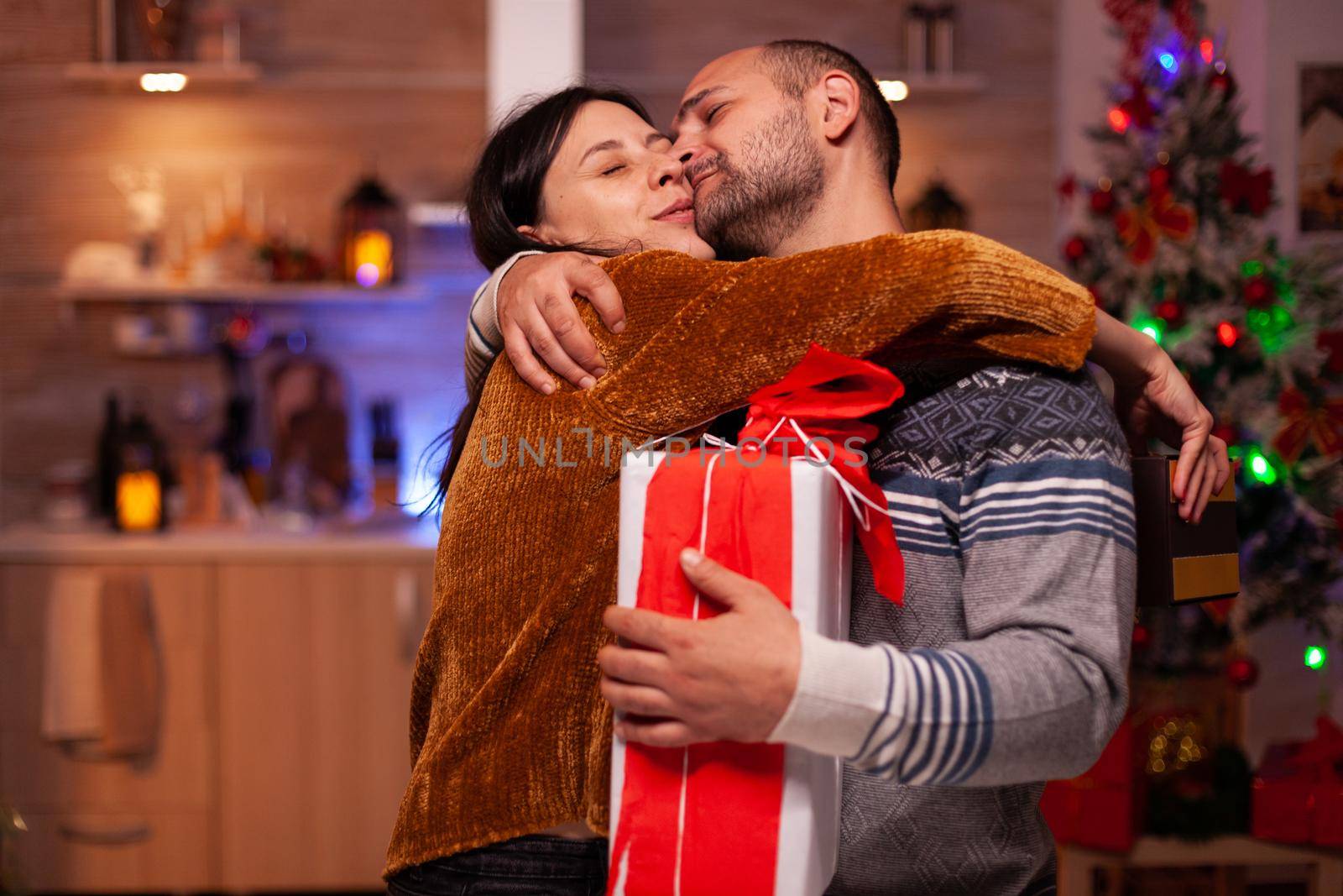 Happy family enjoying spending time together during christmas holiday holding xmas decorated present gift with ribbon on it. Excited married couple hugging celebrating winter festive season