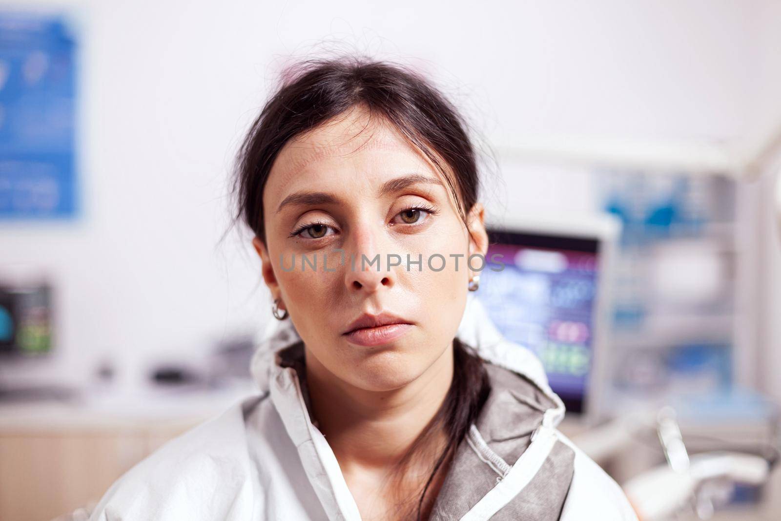 Exhausted dentist wearing protective gear agasint coronavirus looking at camera. Tired medical specialist in dentistry cabinet wearing safety equipment during global health crisis.