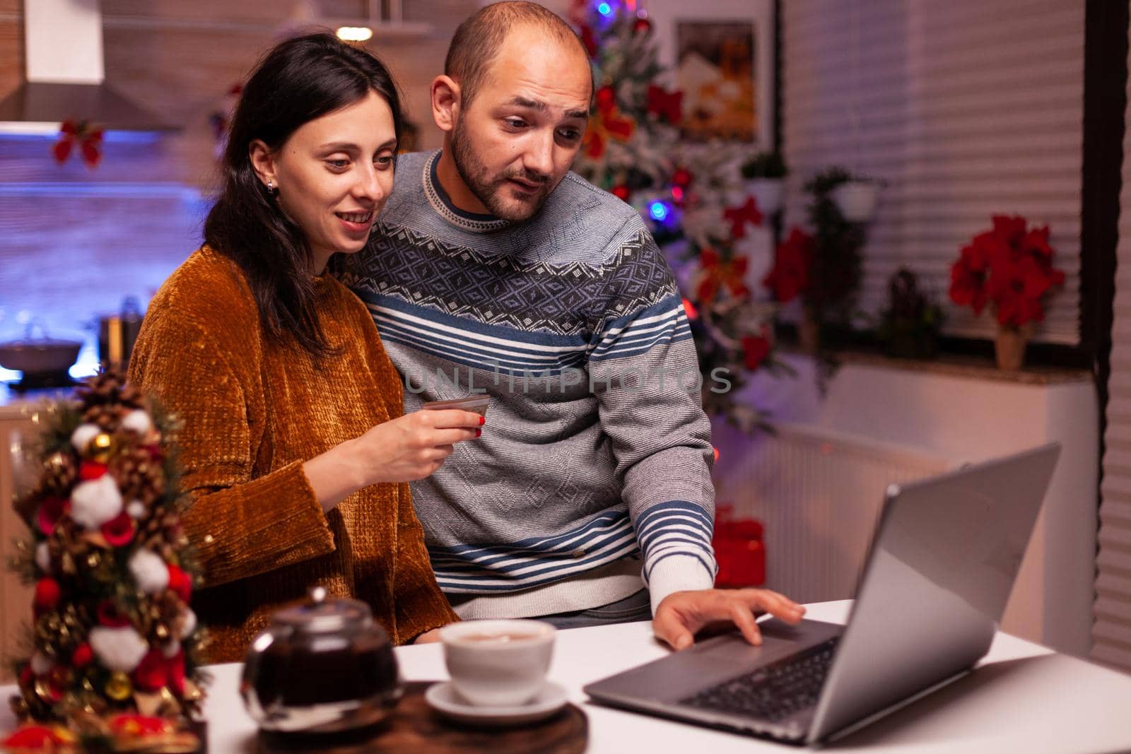 Happy family doing online shopping buying xmas present using credit card making transaction using laptop computer x-mas decorated kitchen. Cheerful family celebrating christmas holiday season together