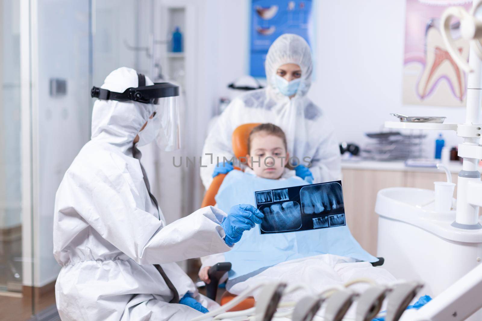 Child and mother in ppe suit listening dentist by DCStudio