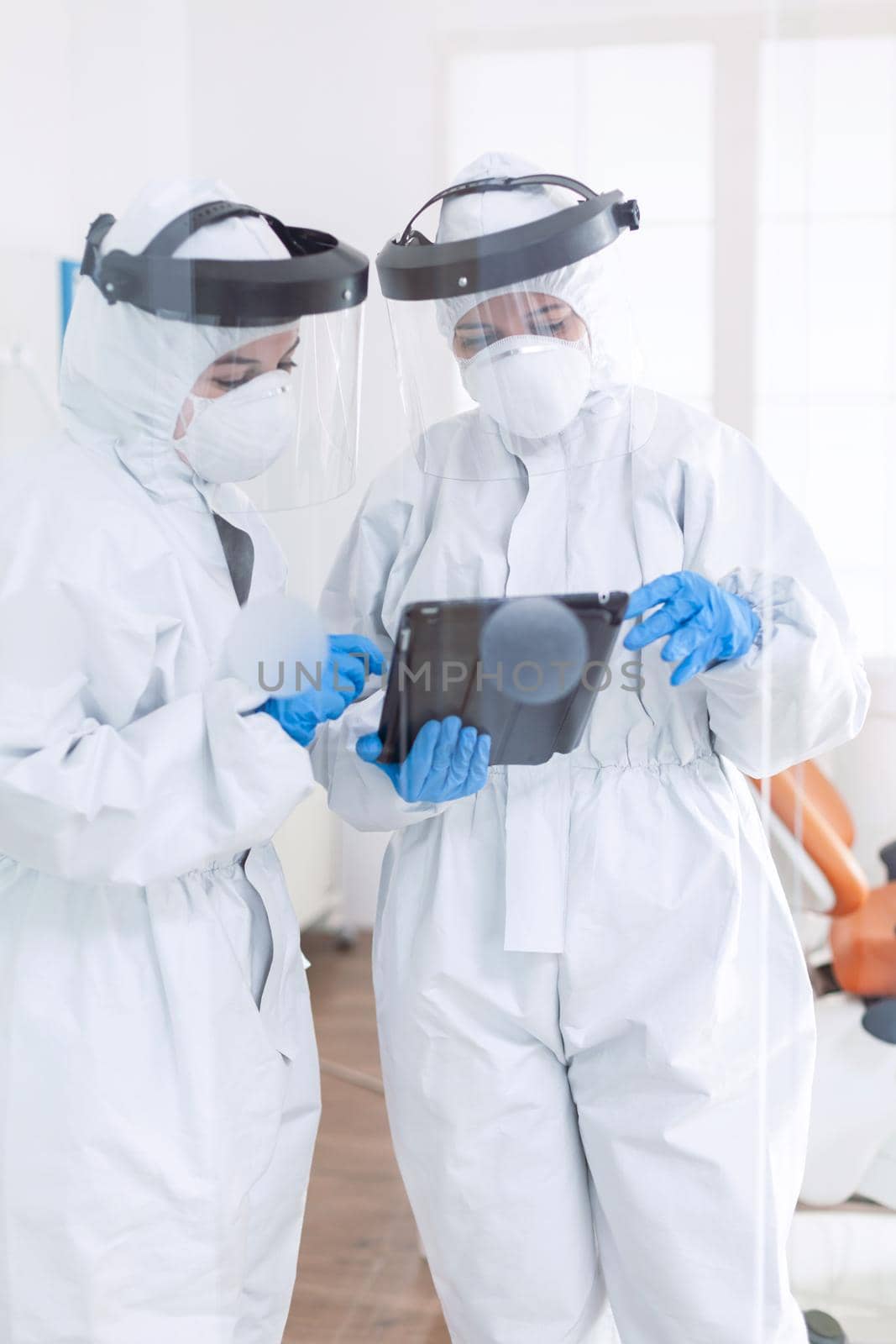 Stressed doctors dressed in ppe suit using tablet pc Stomatology team in dental office wearing protective suit agasint contagious coronavirus during global pandemic.